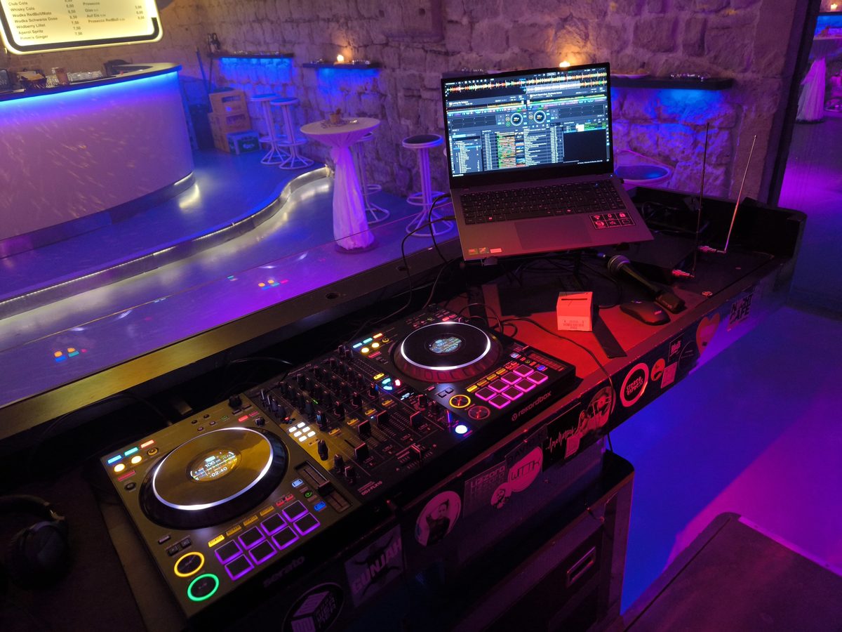 DJ-Pult mit Laptop vor einer beleuchteten Bar im Gewölbekeller