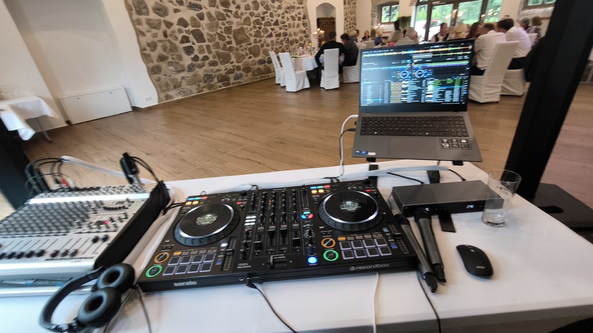 DJ-Pult mit Mischpult und Laptop, im Hintergrund die festlich gedeckte Hochzeitsgesellschaft