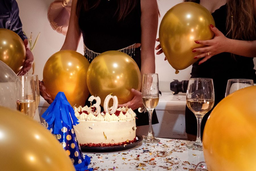 Geburtstagstorte mit Zahlenkerze 30, goldene Luftballons und Sektgläser